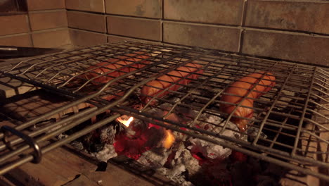 handheld shot of sausages on a charcoal bbq at night creating flames from the dripping fat from right hand side