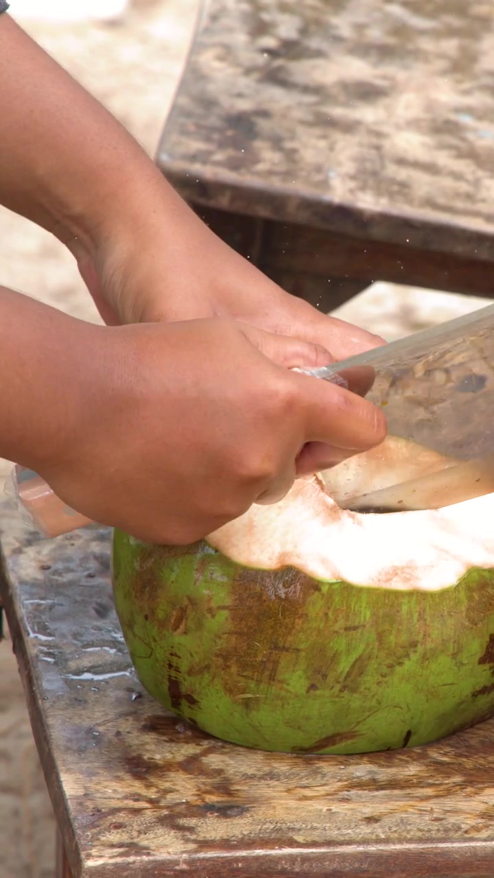 Close-up shot of hands skillfully chopping a green coconut with a cleaver outdoors