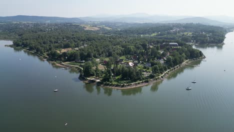 línea de costa del sereno lago de montaña en las montañas beskid, rodeado de vegetación durante un día de verano - vista aérea 4k