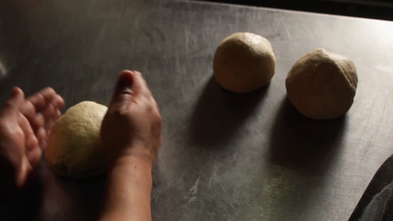 a female chef deflating three pieces of round pizza dough