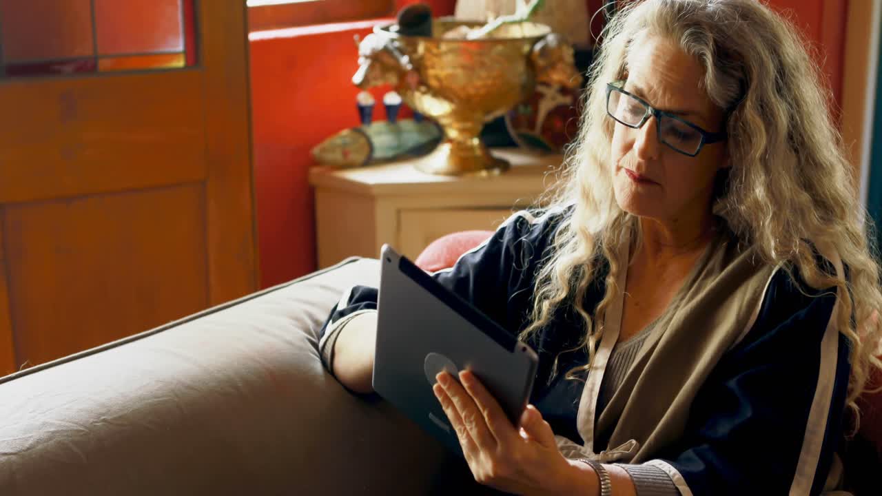 Femme mature utilisant une tablette numérique dans le salon 4k