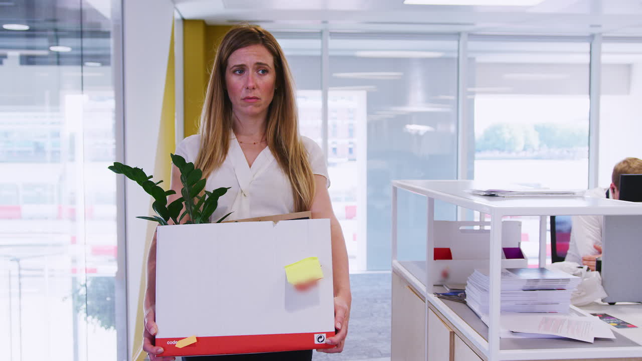 Young woman holding box of her belongings leaving an office