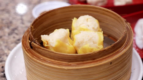 picking a steaming dumpling using chopsticks and dipping it into a spicy sauce, while eating in a chinese restaurant in bangkok, thailand