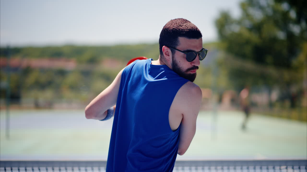 Close up of a man in a blue shirt playing pickleball with a red racket on a sunny day