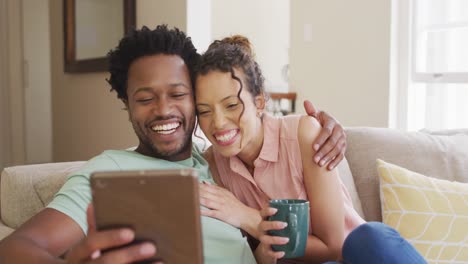 happy biracial couple sitting on sofa and having video call on smartphone