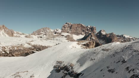 Dolly-back-drone-shot-of-hiker-walking-along-a-steep-snowy-ridge