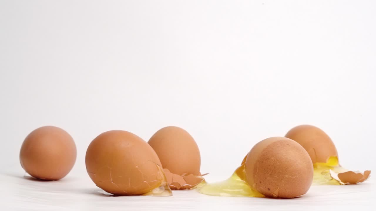 Brown eggs dropped and breaking on white studio backdrop in 4k slow motion