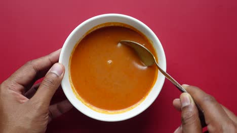 hands holding a bowl of orange-red soup with spoon