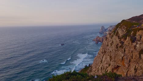 Steep-rocky-coastline-overseeing-waves-of-ocean-tide-approaching,-handheld