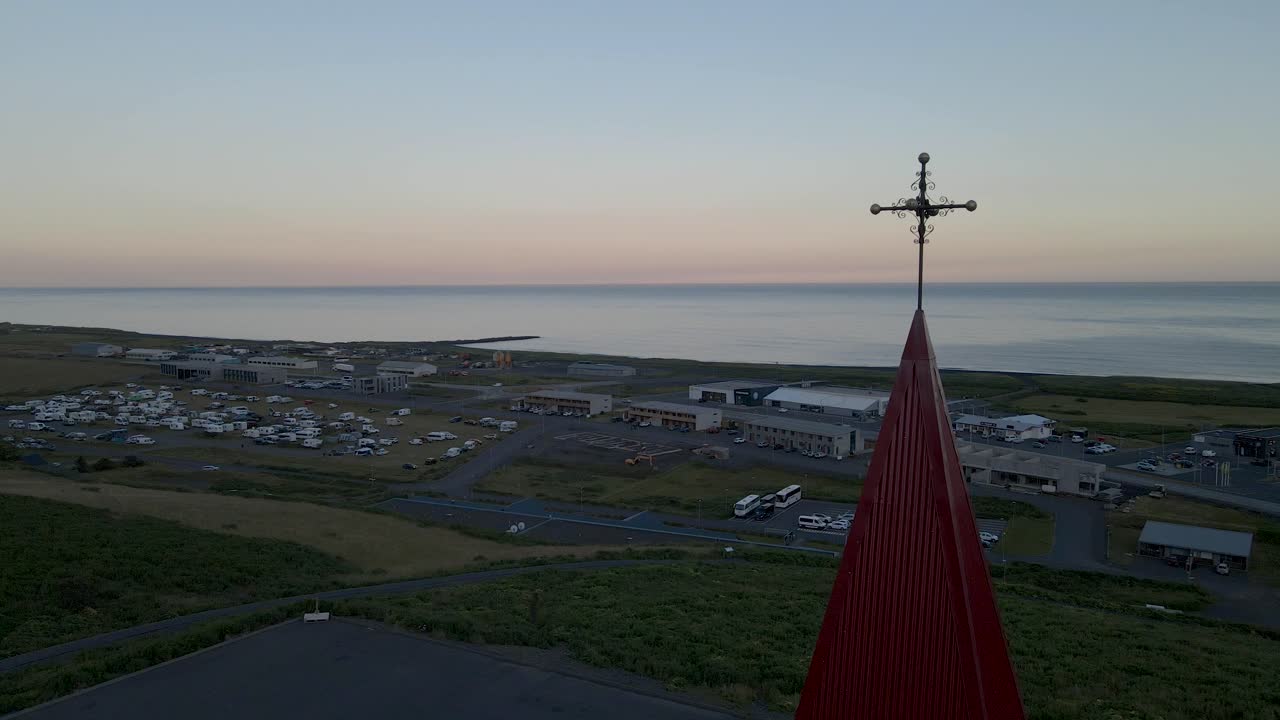 Hover above Vik, Iceland, as our drone captures a close shot of the top of Reyniskirkja Church's striking white and red facade, perched prominently on a hill overseeing the town below