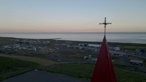Hover above Vik, Iceland, as our drone captures a close shot of the top of Reyniskirkja Church&#039;s striking white and red facade, perched prominently on a hill overseeing the town below