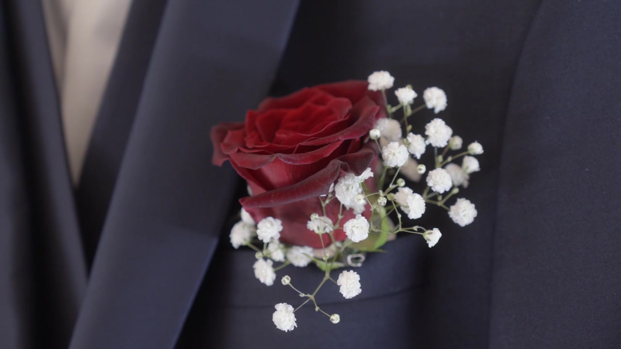 Boutonnière de rosa vermelha com flores de mosquitinhos brancos presa ao terno de casamento formal escuro de um noivo