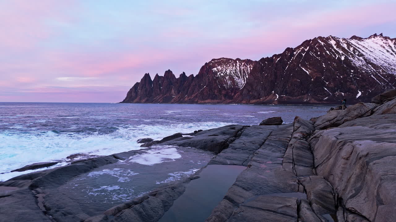 Littoral rocheux de la plage de Tungeneset, Senja, avec des montagnes déchiquetées et un ciel rose au coucher du soleil