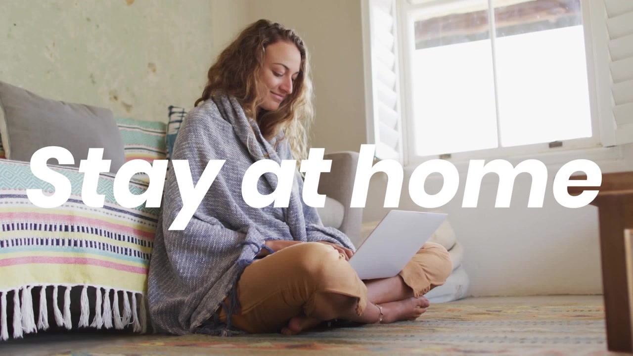 Animasjon av «stay at home»-tekst over kaukasisk kvinne som bruker laptop hjemme