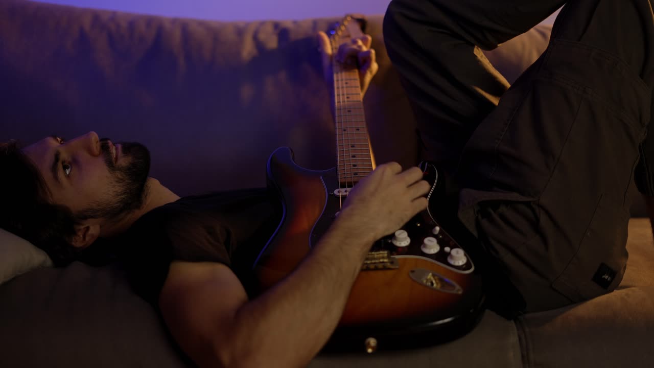 Inspired Man composing music on guitar while lying on couch