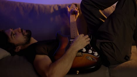 hombre inspirado componiendo música en la guitarra mientras está acostado en el sofá