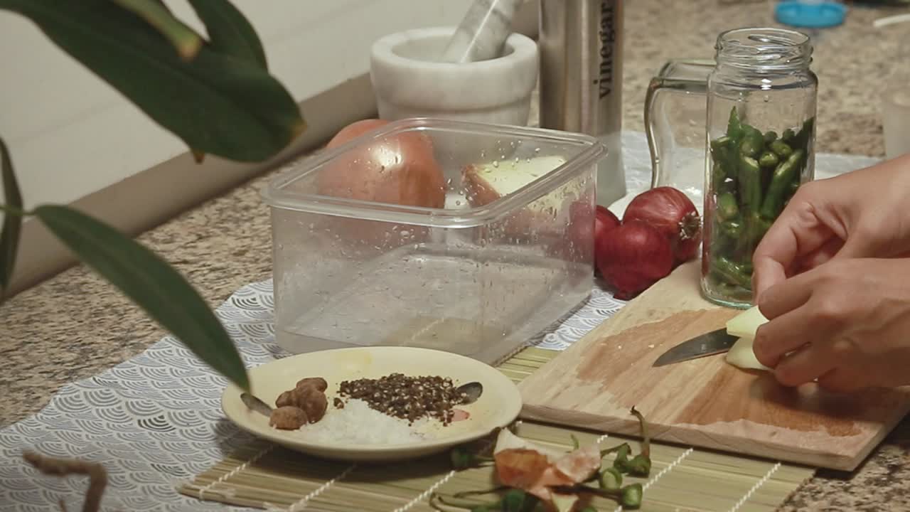 Candid kitchen scene of chopping and adding white onions to a jar of green chili to make healthy pickles