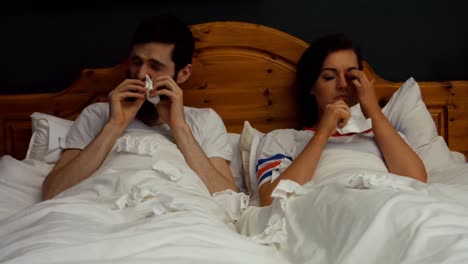 Couple-covering-nose-while-sneezing-on-bed