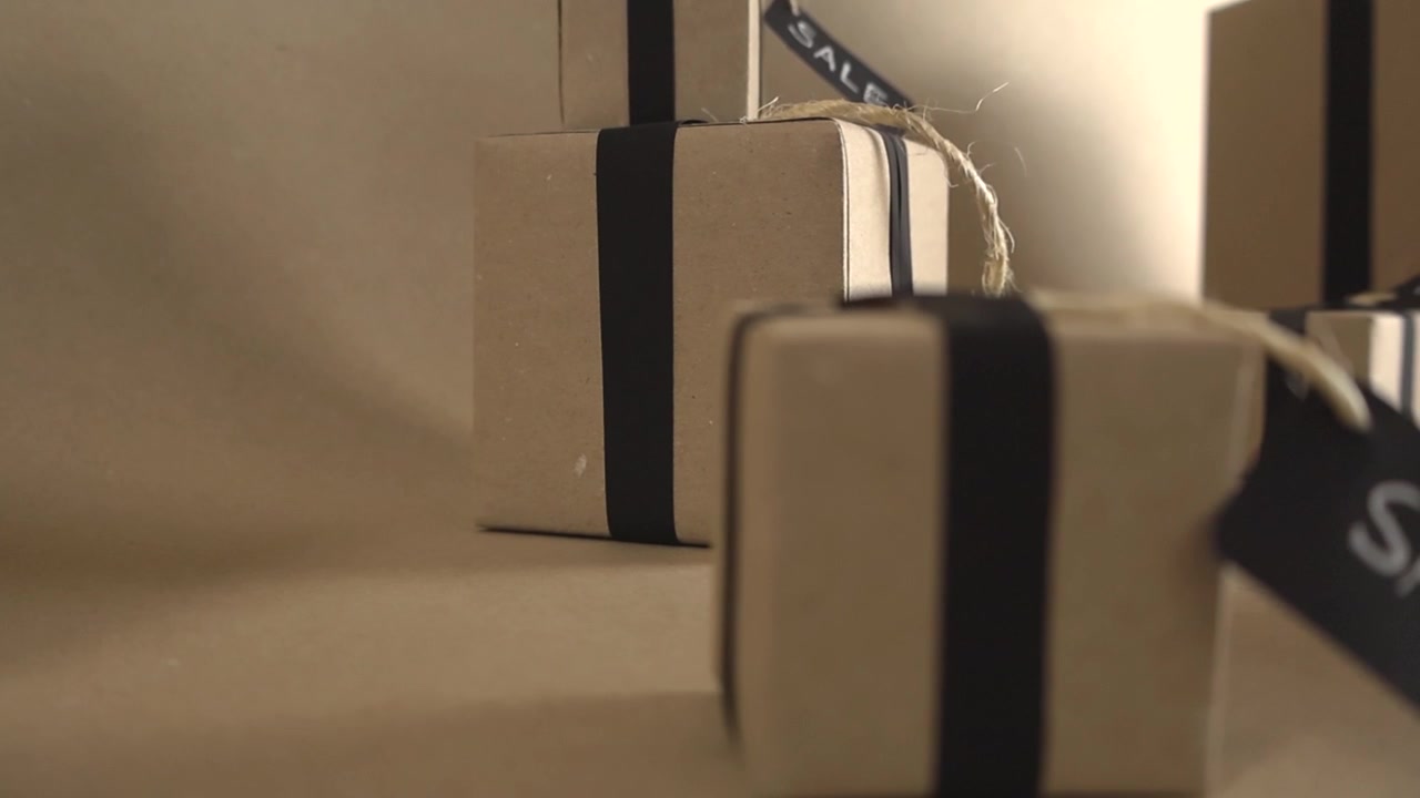 Numerose scatole regalo di cartone con nastri neri e cartellini di vendita su uno sfondo marrone chiaro. Concetto perfetto per Black Friday, Cyber Monday, promozioni, sconti e offerte speciali.