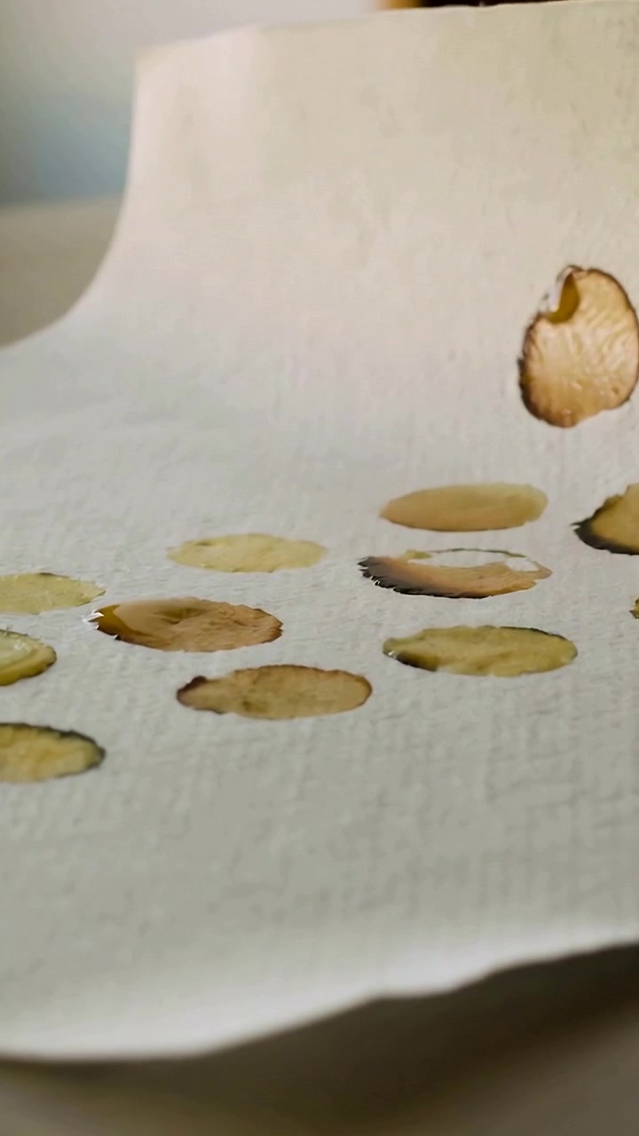 Video verticale: Il bordo sinistro solleva un foglio assorbente sul tavolo, rivelando cerchi bagnati e accumuli d'acqua