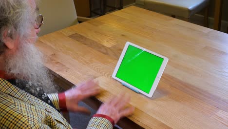 un hombre mayor con barba hablando con una tableta con pantalla verde