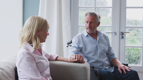 senior couple with man in wheelchair sitting in lounge at home talking and laughing together