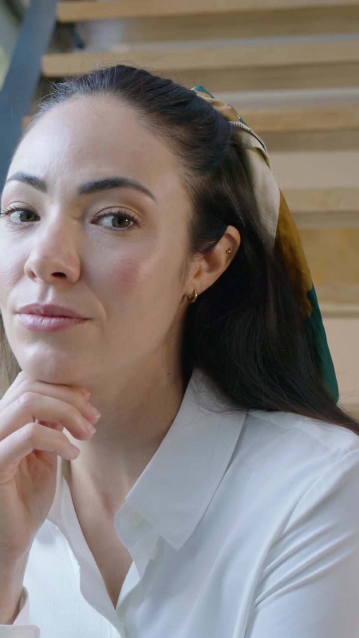Video verticale: Zoom su una donna con sciarpa che le sostiene il mento, che pensa e sposta lo sguardo sulle scale.