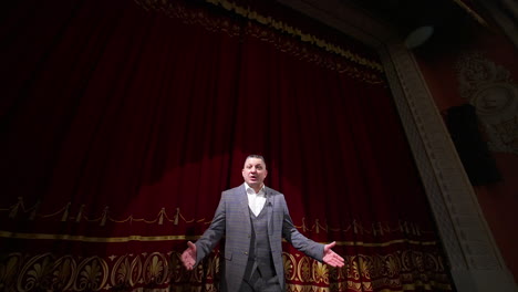 theater host on red curtains background. man in grey costume talking on a big stage. portrait of an actor performing on stage.