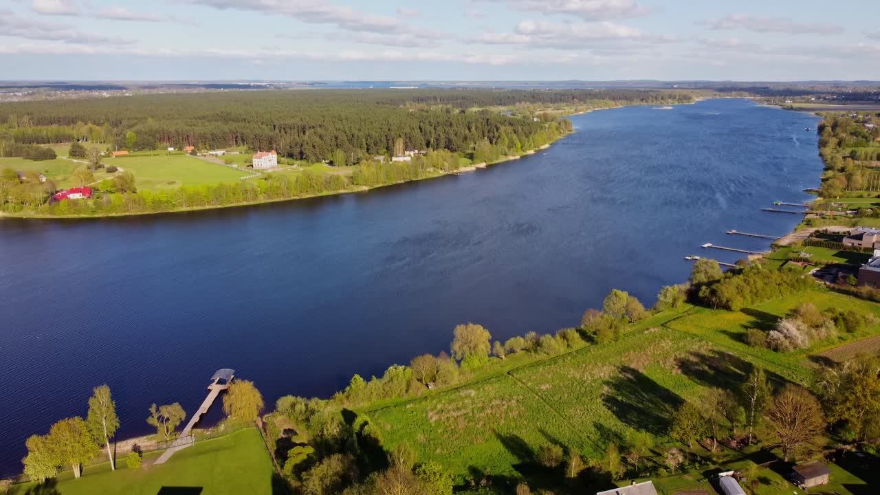 A big river winds through Katlakalns residential area, surrounded by spring nature and homes
