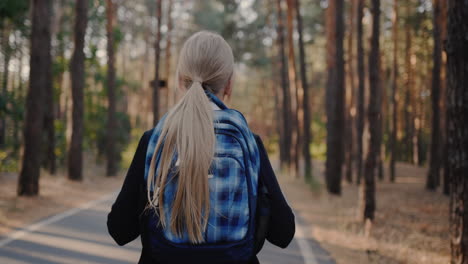 a child with a back pack walks alone through a park with tall trees