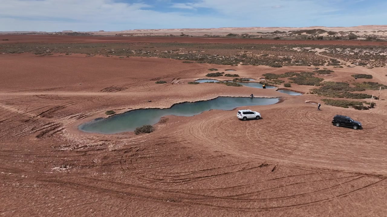 Vista aerea con drone di visitatori fuoristrada che esplorano le piscine naturali nel deserto vicino a Dakhla, una destinazione di ecoturismo unica nel Sahara Atlantico del Marocco, accessibile con veicoli a trazione integrale