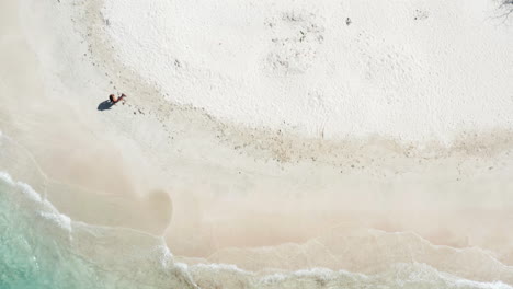 Aerial-crane-up-revealing-single-woman-walking-on-deserted-tropical-beach,-solo-travel-concept