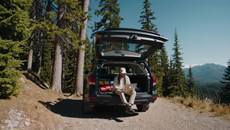 man working remotely from car trunk in scenic mountain forest
