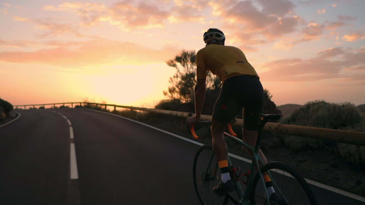A young sports man riding a bike on a mountain serpentine in a yellow t-shirt helmet and sports equipment rear view . Slow motion steadicam