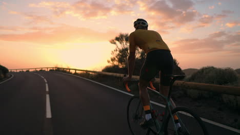 a young sports man riding a bike on a mountain serpentine in a yellow t-shirt helmet and sports equipment rear view . slow motion steadicam