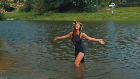 young female with floral wreath standing in lake water and raising hands to sky