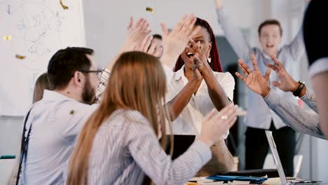 happy young african american female boss celebrating success with multiethnic team, confetti falling at office meeting.