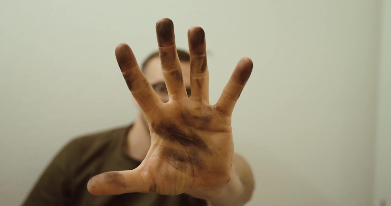 Primo piano di una mano sporca tenuta verso la telecamera su uno sfondo bianco pulito. Forte contrasto che evidenzia il lavoro manuale, il lavoro, lo sporco e le condizioni di lavoro reali.