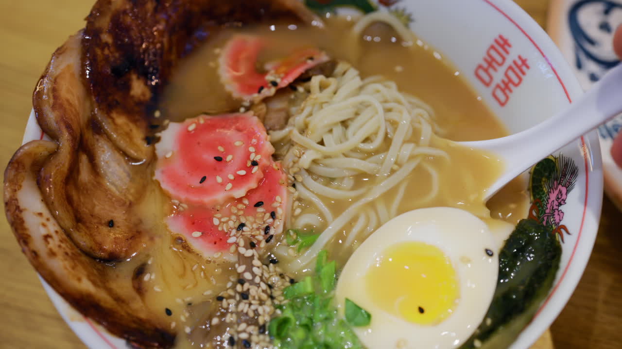 Primo piano di un cucchiaio che solleva ramen mostrando i condimenti e il brodo fumante