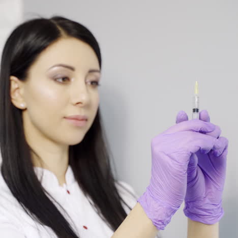 A beautiful cosmetologist with long hair checks the syringe with an injection before administering the drug to the client in the beauty salon. Aesthetic cosmetology. Close-up.