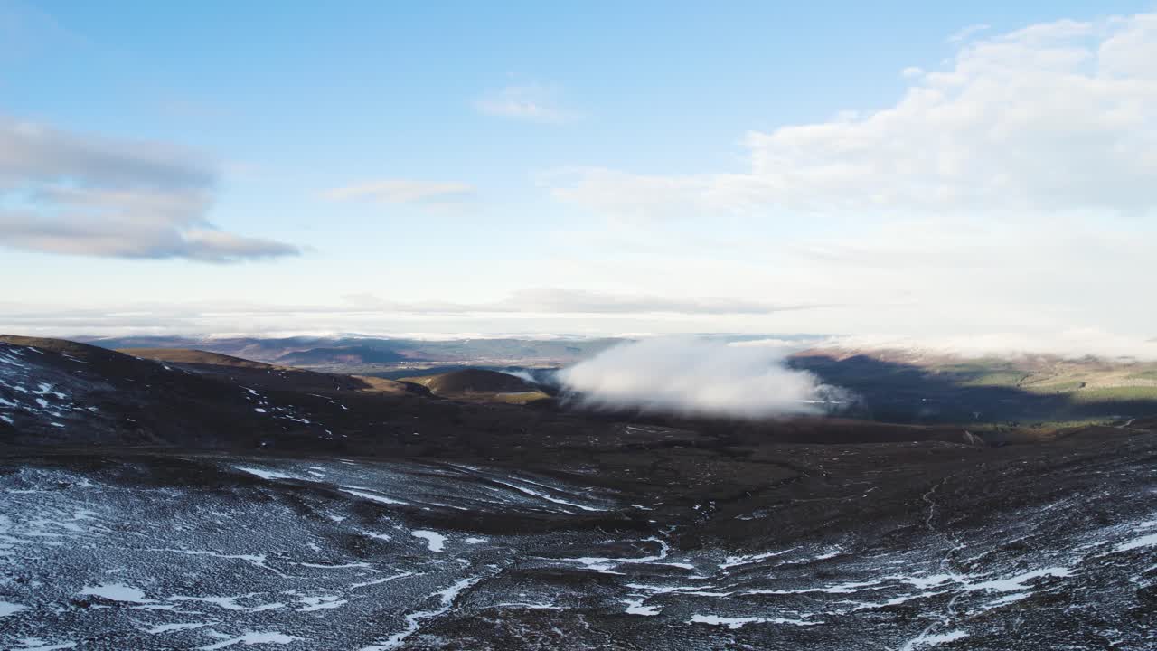 Aerial drone footage in winter filmed in Coire an t-Sneachda in the Cairngroms National Park in Scotland with patchy snow, mountains and clouds facing Aviemore and Glen More with an icy path