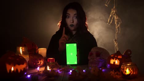 woman holds smartphone in vertical orientation with green screen and points on it by her finger