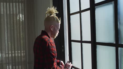 thoughtful albino african american man with dreadlocks looking at the window