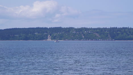 Distant-sailboat-motoring-past-beach-at-Camano-Island-State-Park,-Washington-State-10sec-24fps-slow-motion