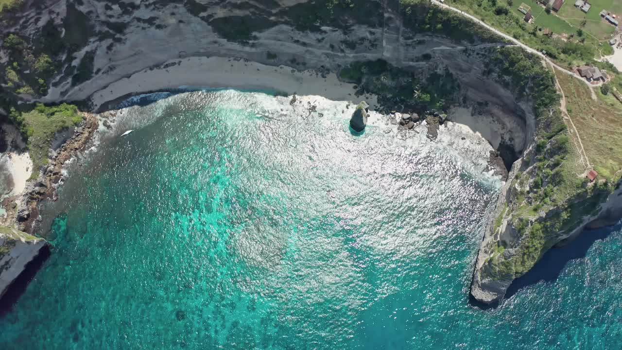 A stunning, high-angle aerial drone shot reveals the pristine white sands, dramatic towering limestone cliffs, and the vibrant turquoise water of Diamond Beach on Nusa Penida island, Bali, Indonesia