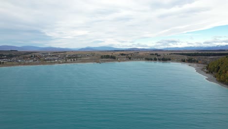 Blue Waters Of Lake Tekapo With Townscape Along Shore In Background. Canterbury, South Island, New Zealand. wide aerial shot