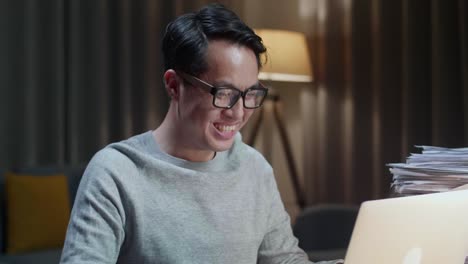 close up of asian man having video call on laptop while working with documents at home