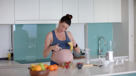 preparing healthy snack, pregnant woman holding banana and smiling in kitchen