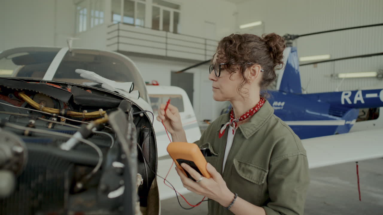 Female Technician Inspecting Aircraft Engine with Digital Multimeter in Hangar