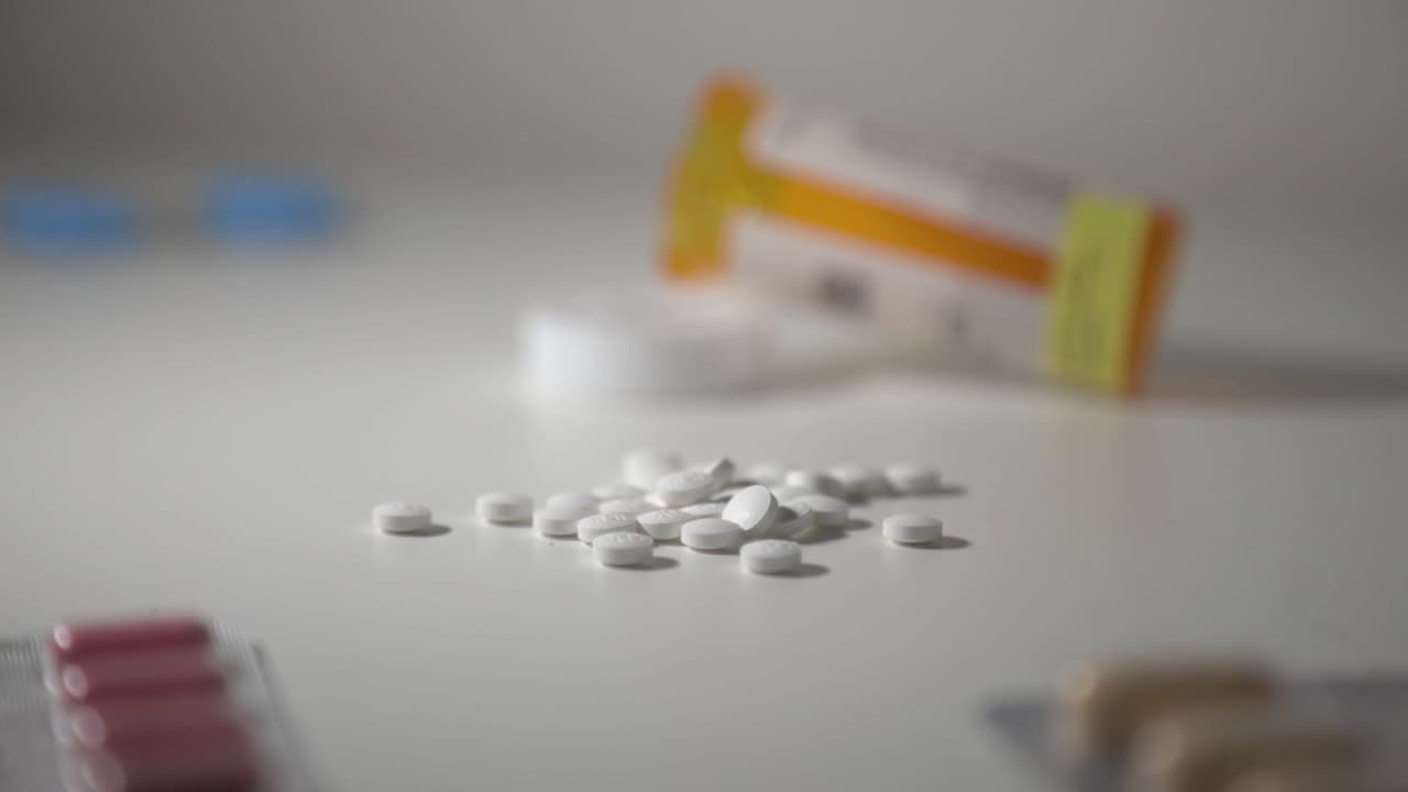 Empty Medicine Bottle Of White Round Pills And Foil Blister Packs Of Capsule Scattered On A Table With White Isolated Background - Medium Panning Shot